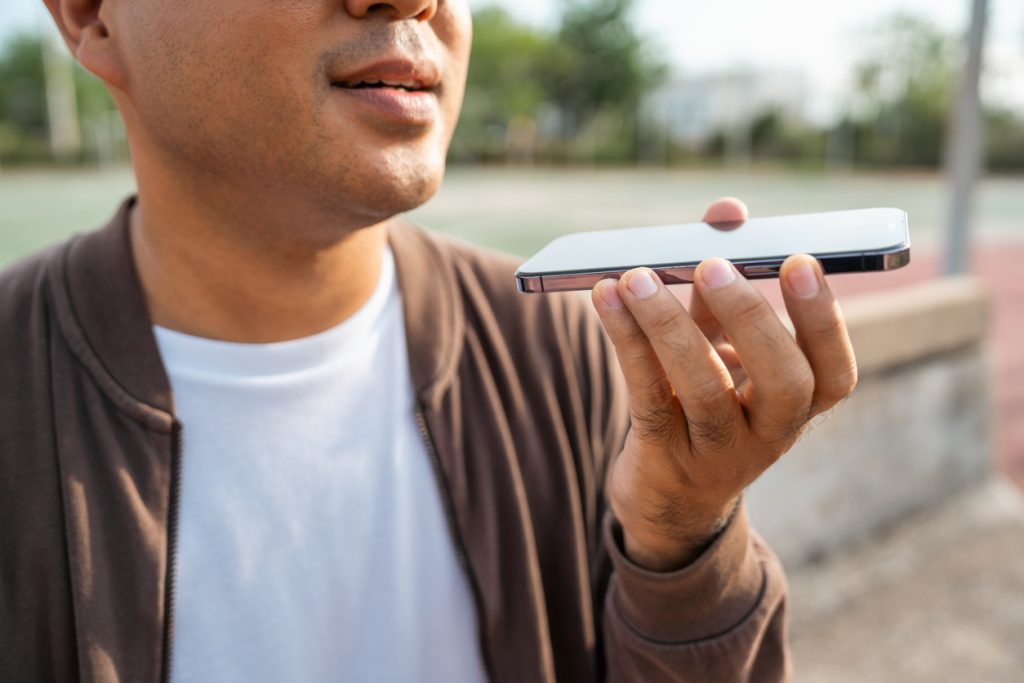 A young man uses voice search on his smartphone. Voice search optimization is critical to SEO.